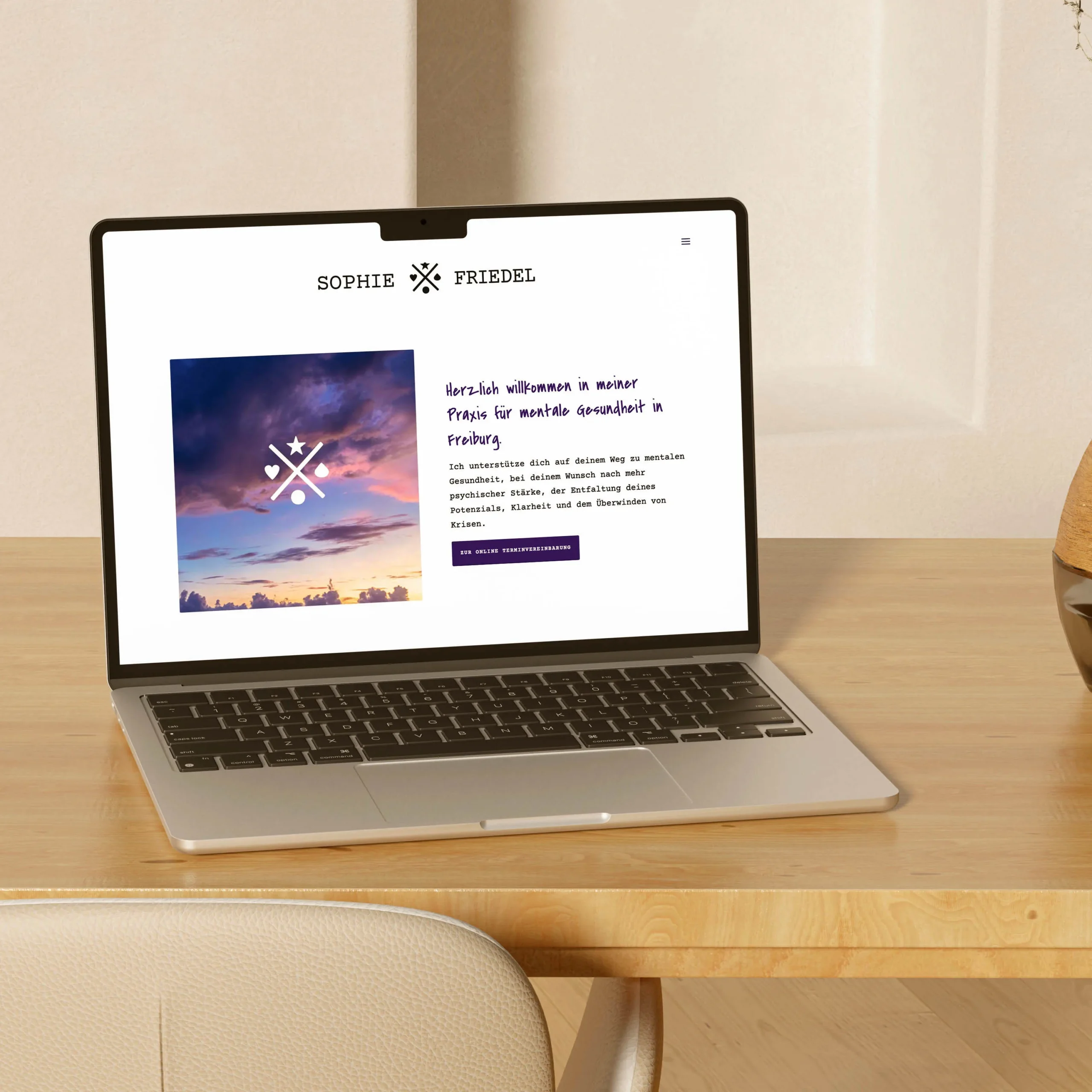 Ein Laptop auf einem Holzschreibtisch, der die Website von Sophie Friedel zeigt. Die Website hat ein minimalistisches Design mit klarer Typografie, einem Bild eines farbenfrohen Himmels und dem Logo von Sophie Friedel. Daneben eine helle Vase und dekorative Elemente.